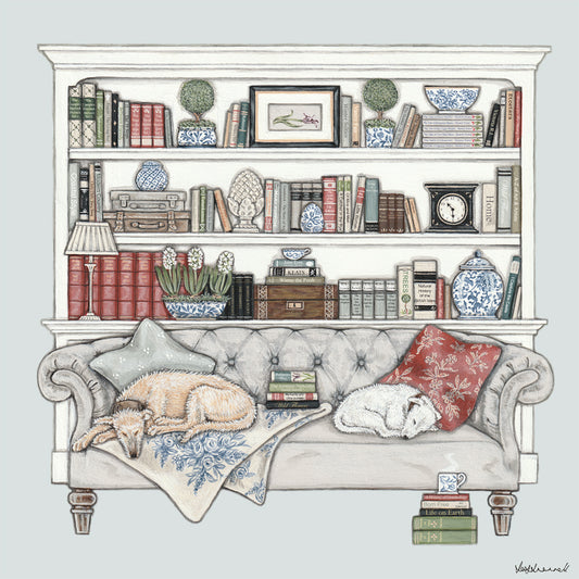 A giclee print featuring 2 sleeping dogs on a chesterfield style sofa infront of book shelves containing old books, blue and white china, a clock, a lamp and a picture.