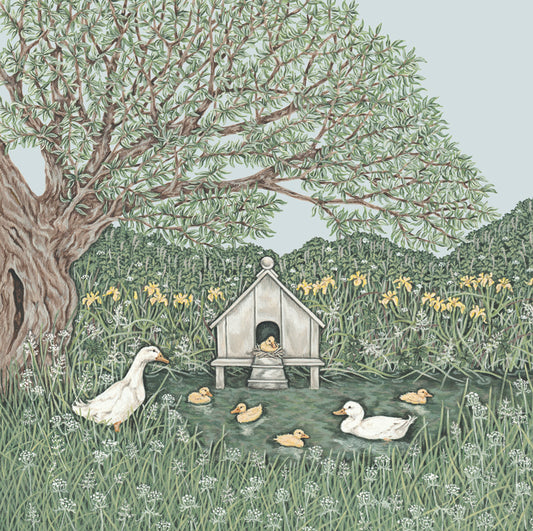 A greetings card featuring a pond containing a swimming white mother duck and her yellow ducklings. A white duck is on the grassy bank under a willow tree. Yellow irises in the background.