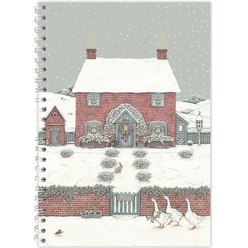 A spiral-bound notebook featuring a winter illustration of a red brick cottage with a snow-covered roof, decorated for Christmas, with geese walking along the lane in the foreground.