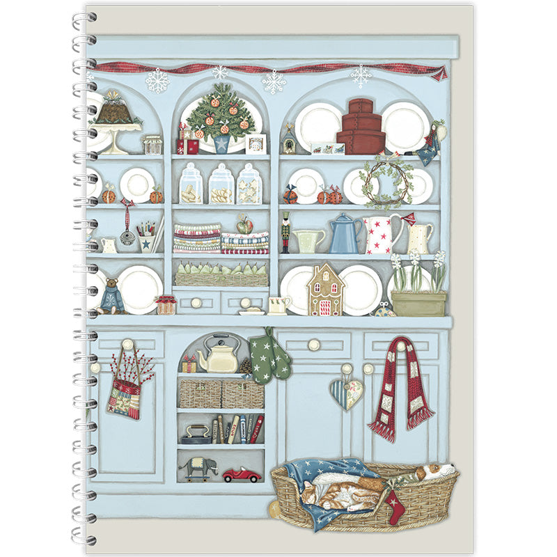 A notebook with a Christmas desser design on the cover, featuring shelves  brimming with traditional crockery, seasonal decorations and cosy Christmas details.