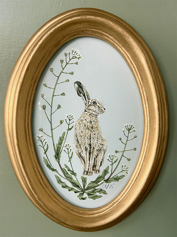 Oval-framed artwork by Sally Swannell of a Hare among Shepherd's Purse on a light blue background