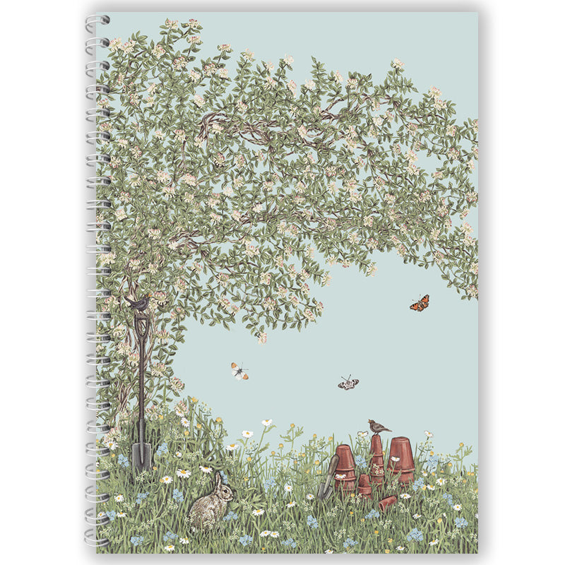 Notebook cover with a garden scene featuring a tree, flowers, and animals on a light blue background.