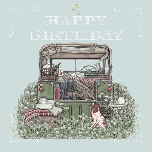 A beautifully illustrated birthday card depicting the open back of a landrover containing a picnic, chairs and boots. A spaniel sits expectantly to the side.